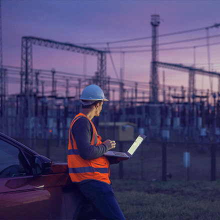 Technik kontroluje energetickú infraštruktúru pri vysokonapäťových vedeniach, symbolizujúc požiadavky NIS2 na kybernetickú bezpečnosť v sektore energetiky.